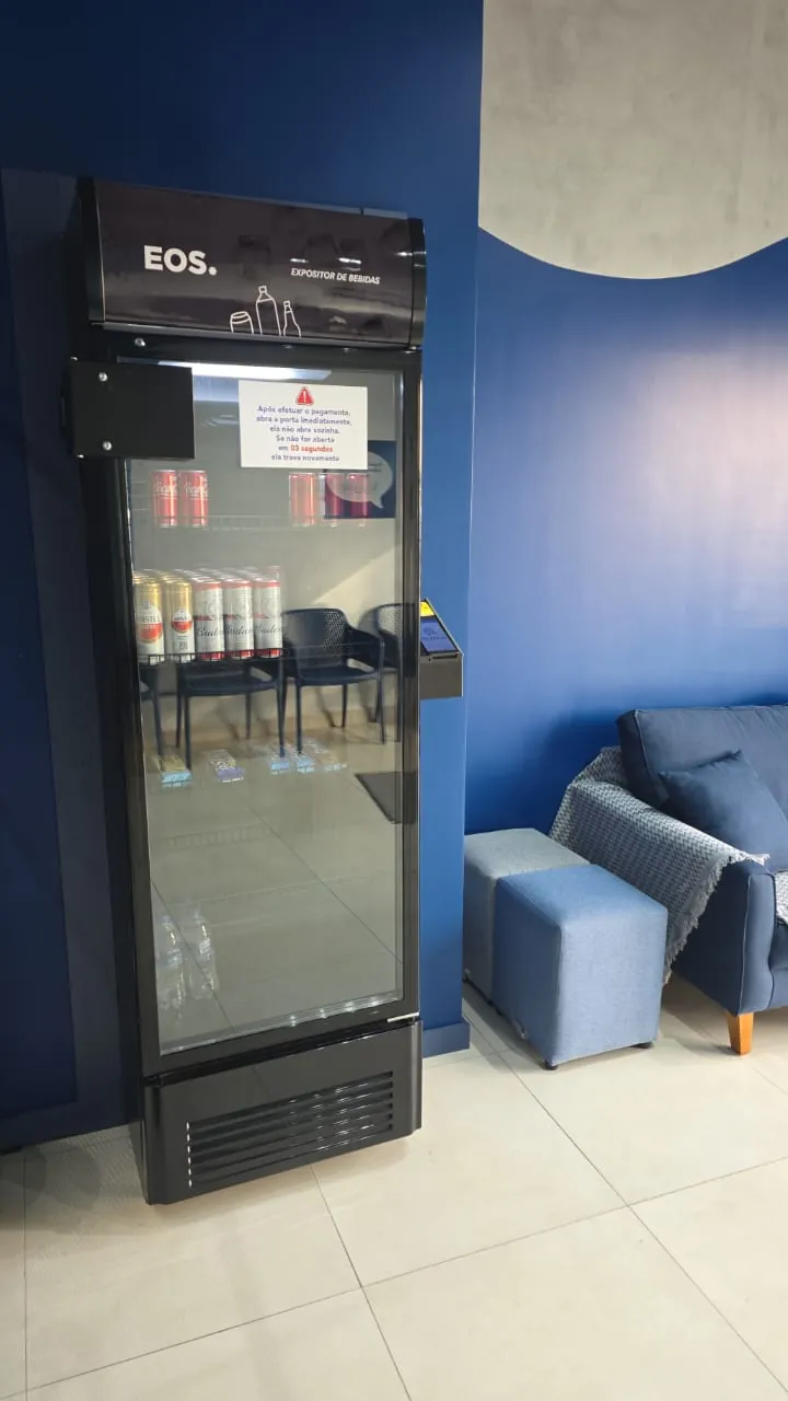 Geladeira de bebidas da Leve & Lave com água, refrigerante e cerveja, ao lado do sofá azul da sala de espera.